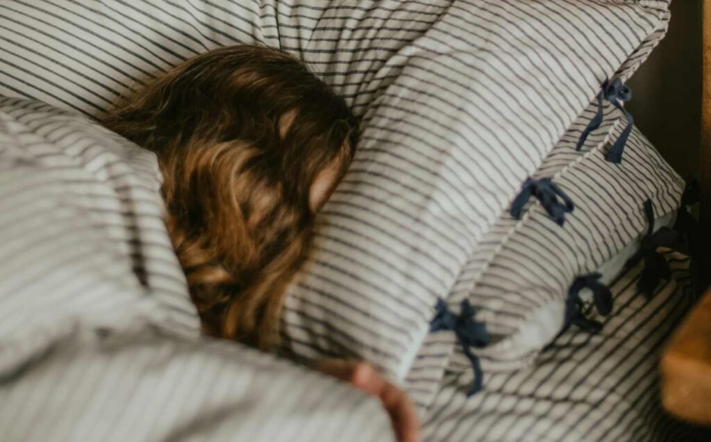 The head and shoulders of a young girl sleeping, on stripped pillow case and sheets. Childhood sleep quality is so important.