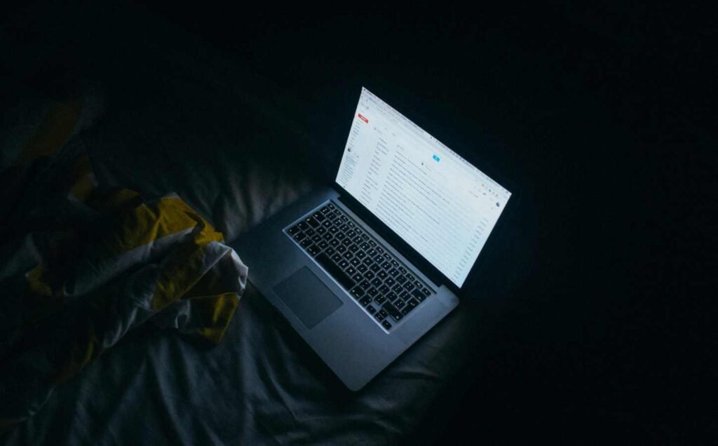 An image of a laptop on a bed at night, the light from the screen illuminates the bedding depicting how blue light affects sleep.