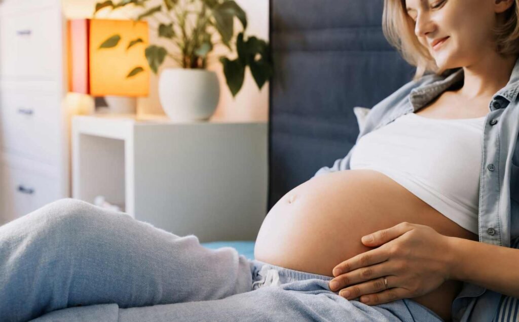 A pregnant woman sitting up with her belly exposed. Enhancing Sleep Quality During Pregnancy. Managing sleeplessness during pregnancy.