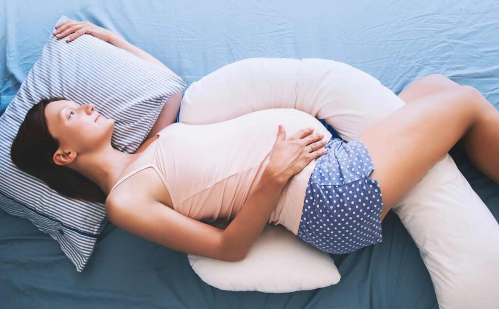 A pregnant woman laying on her side, she is wearing blue and white polka dot shorts and a pink singlet. For the recommended sleep position for women section.