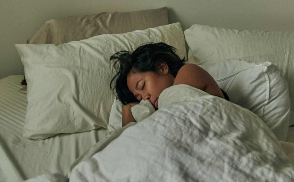 A woman asleep in a bed with white linen bedding. For the beneficial foods that promote good sleep section.