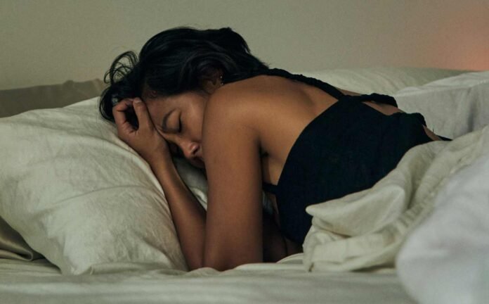 A woman laying face down in bed. She is wearing a black nightdress. How Your Diet Impacts Sleep Quality