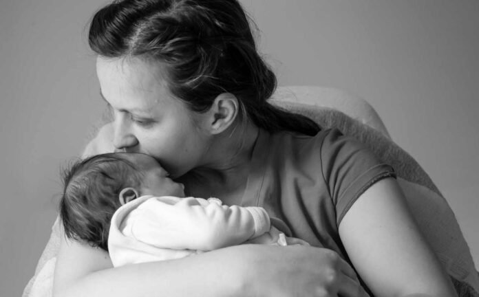 A black and white photo of a mother kissing her baby on the forehead in a soothing way.