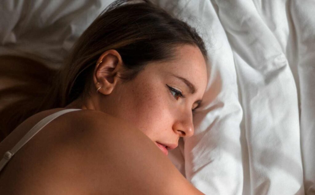 A young lady laying on white sheets awake, for the best and worst foods for sleep section.