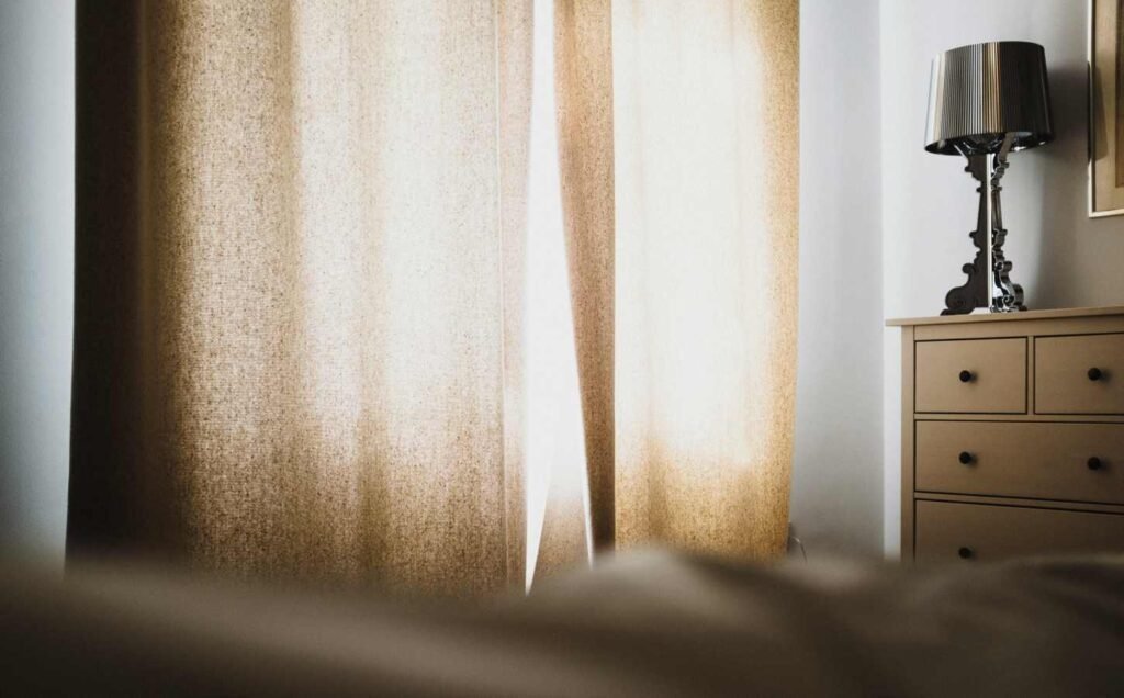 An image of a bedroom with light curtains, illustrating that blackout curtains could be one natural solution for your sleeping problems.