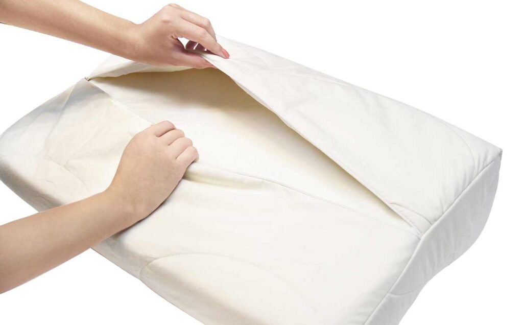 The hands of a person removing the cover of a memory foam pillow. Tips for how to clean a memory foam pillow.