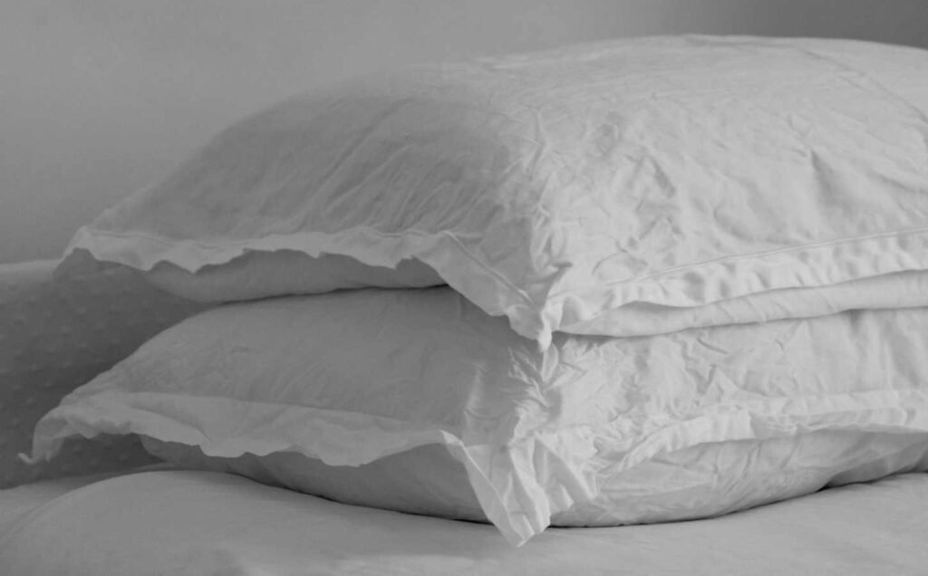 Two pillows in wrinkled linen pillow cases stacked on a bed. Black and white image.