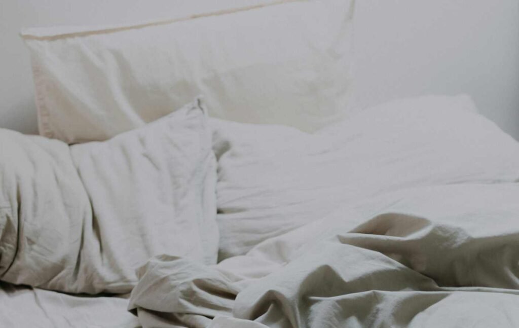 Three white pillows on a bed behind a tossed and wrinkled sheet. How to sanitize pillows.