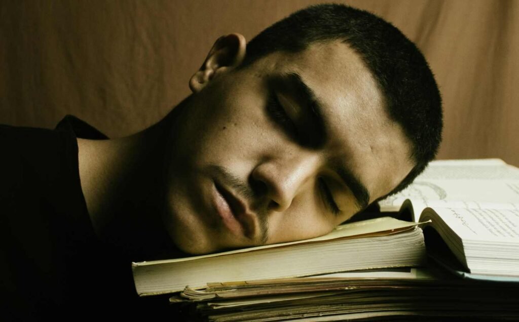 A head and shoulders shot of a man asleep on a pile of books.