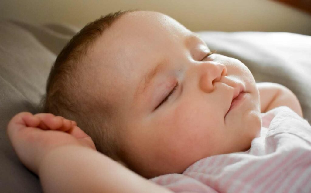 Head and shoulders of a baby sleeping, with his right hand beside his head.