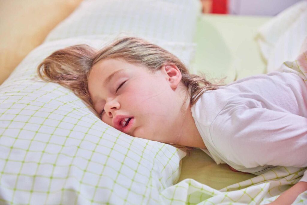 A young girl laying face down asleep and snoring.