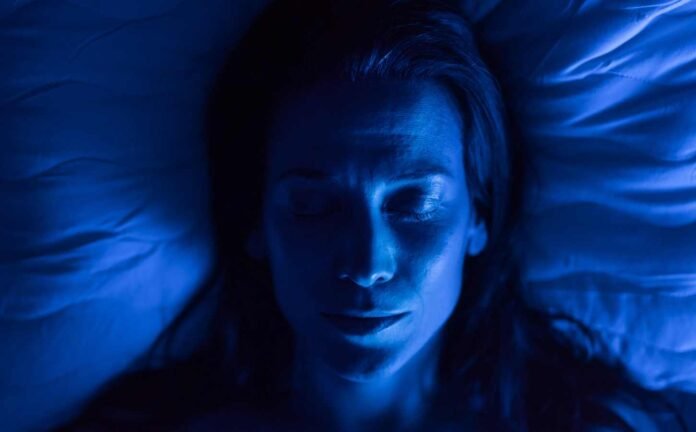 Head and shoulders of a woman sleeping, under a blue light.