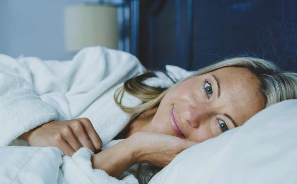 A middle aged woman laying awake on her side looking at the camera. Sleep Health and Anxiety in Midlife Women.