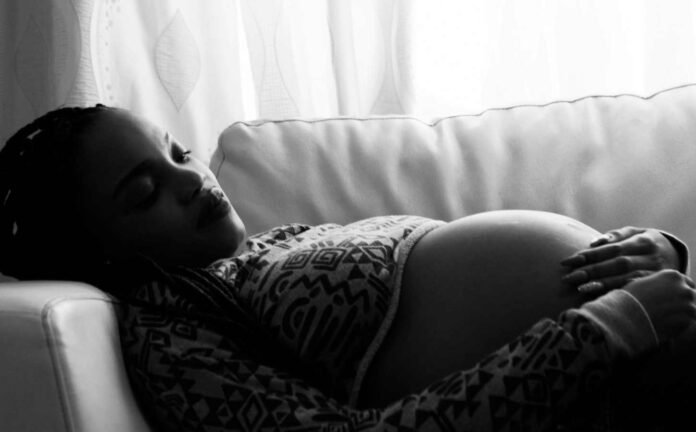 A black and white photo of a pregnant woman laying on a couch.