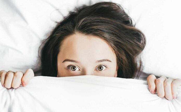 The eyes and forehead of a female peaking out from beneath white sheet, eyes wide open at the Expanding Insomnia Market.