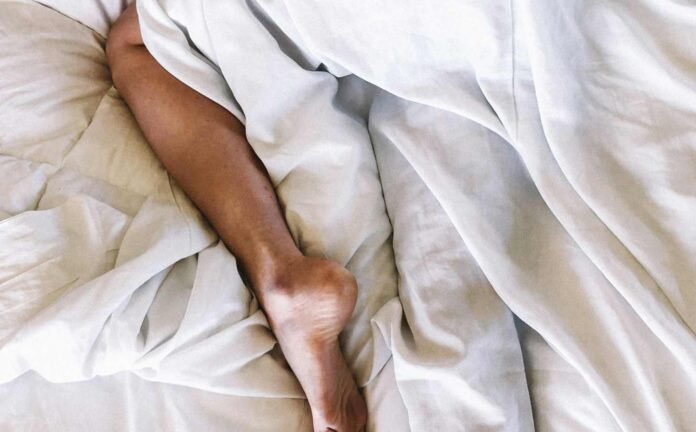 A male laying in bed with the lower portion below the knee exposed. Understanding restless leg syndrome.