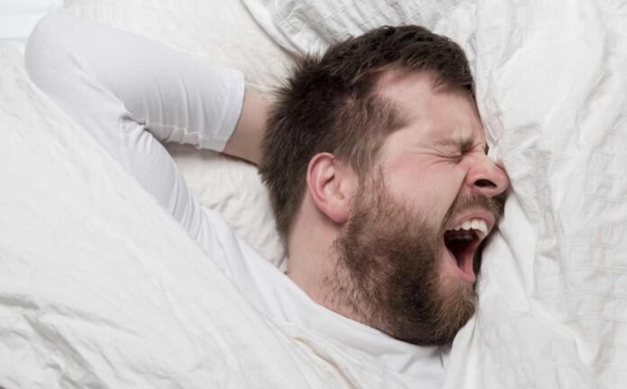 A male in a bed yawing, because he can't sleep