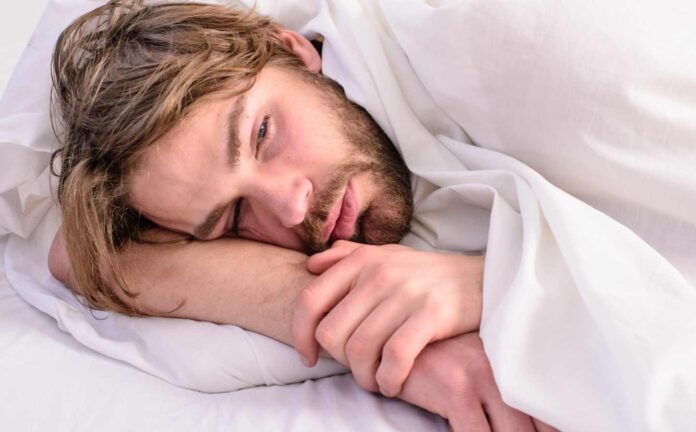 A man laying in a bed with white sheets, unable to sleep.