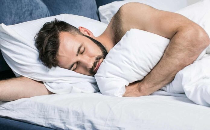 A man sleeping on his side, blue bed base and white sheets.