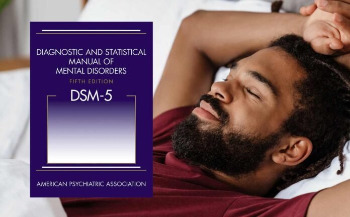 A male sleeping with his hands above his head with a copy of diagnostic and statistical manual of mental disorders in the foreground.