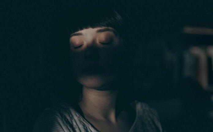 Head and shoulders of a female sitting in the dark experiencing disrupted nighttime sleep.