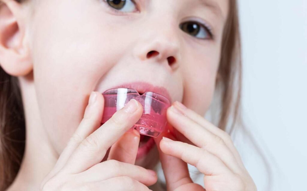 A young girl fitting a myofunctional trainer into her mouth to help strengthen the muscles in the mouth and throat to stop sleep apnea.