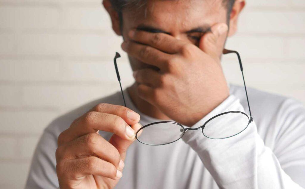 A close up of a man holding his glasses on one hand while he massages his eyes with the other.