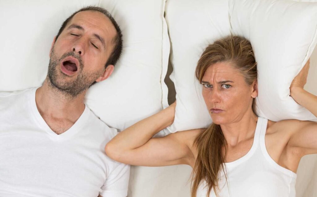 A male and female in bed. The male is snoring and the woman is awake because he is snoring.