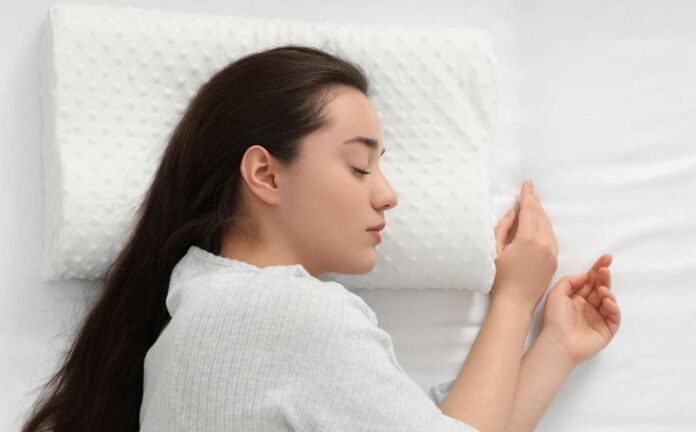 A woman laying in bed asleep on her side, her head on a memory foam pillow.