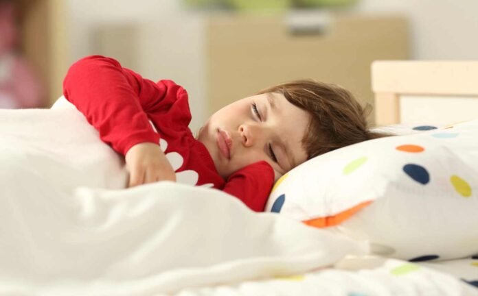 A two year old sleeping in bed wearing a red night shirt.