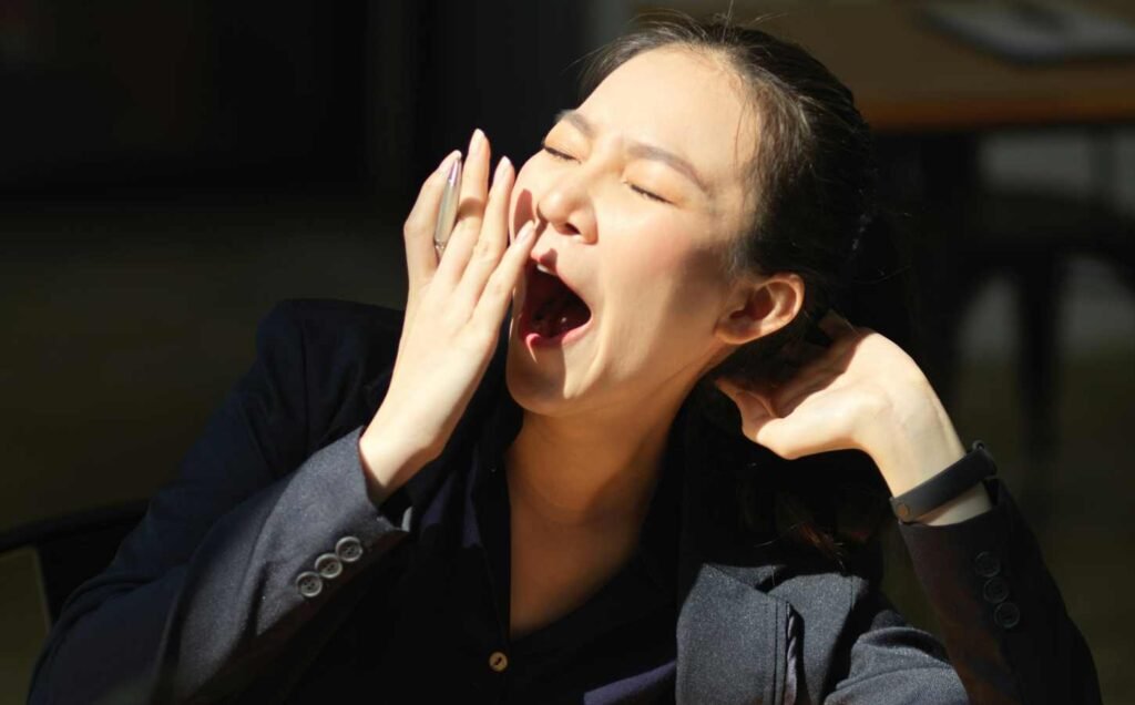 A woman with a hand up to her mouth as she is yawning because she is suffering from Insufficient sleep syndrome.