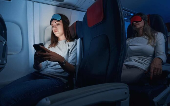 Two woman on an airplane, one asleep while the other is on her iPad. Both are likely to experience jet lag disorder.