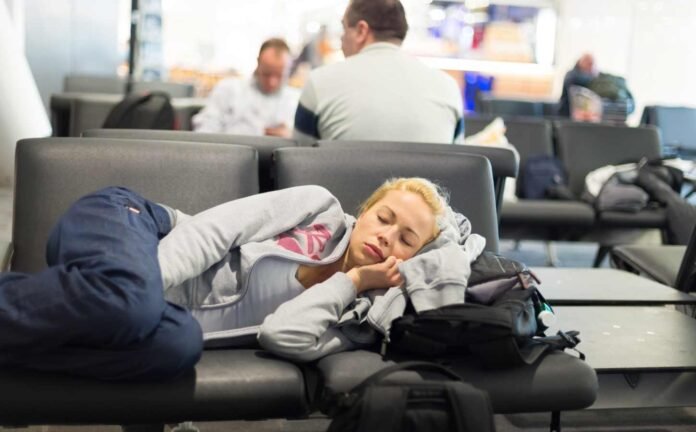 A woman lying across two seats in an airport trying to sleep.