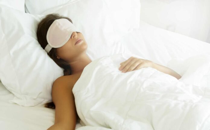 A woman sleeping in a bed with an eye mask on.