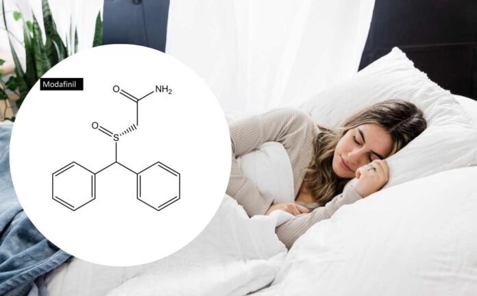 A woman asleep in a bed with white sheets and pillows with a Modafinil molecular structure diagram to one side.