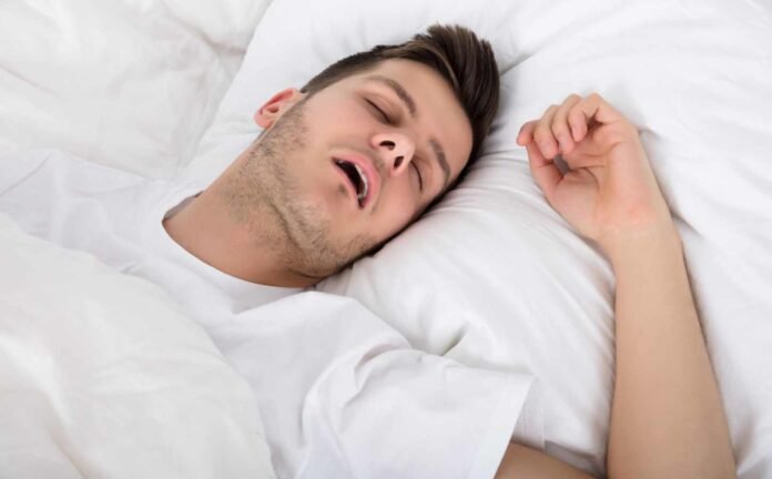 A male in a white t-shirt asleep with his mouth open. Narcolepsy Type 1 symtoms.