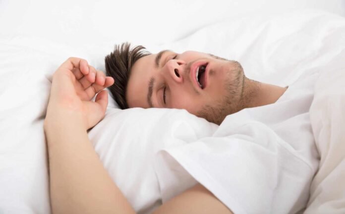 A male in a white t-shirt on white sheets sleeping. Showing signs of Narcolepsy Type 2.