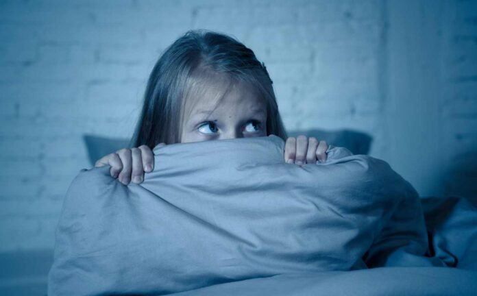 A young girl holding her blankets up to her eyes, afraid of night terrors.