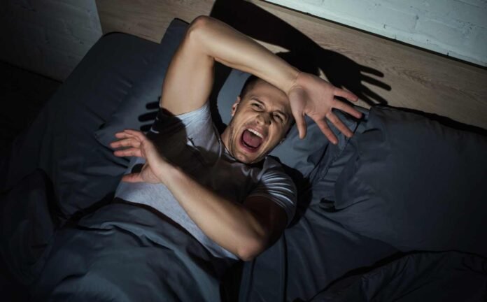 A man in bed with his arms up, experiencing nightmares.