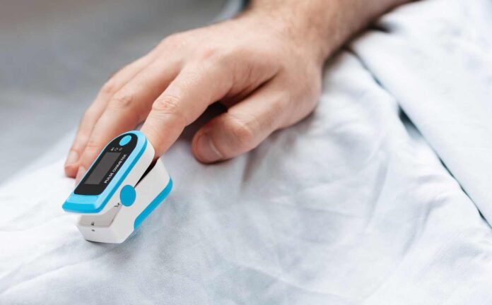 A close up of a mans hand with an oximeter on his index finger.