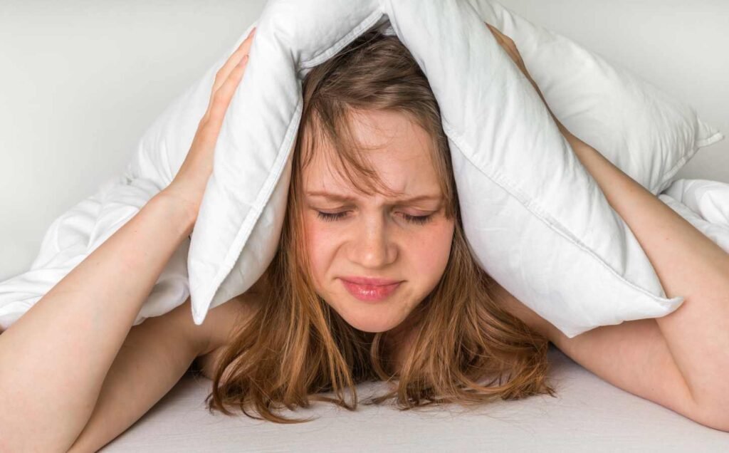 A woman experiencing non-circadian sleep disorder covering her head with a pillow.