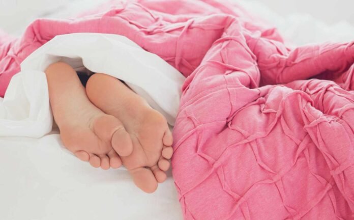 A pair of feet sticking out from under a pink duvet and white sheets, symbolic of periodic limb movement disorder.