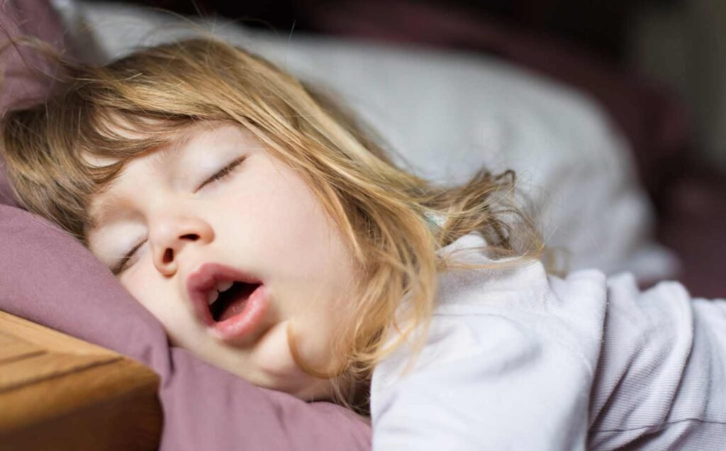 A young girl asleep in bed primary snoring with her mouth open.