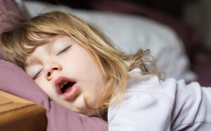 A young girl asleep in bed primary snoring with her mouth open.