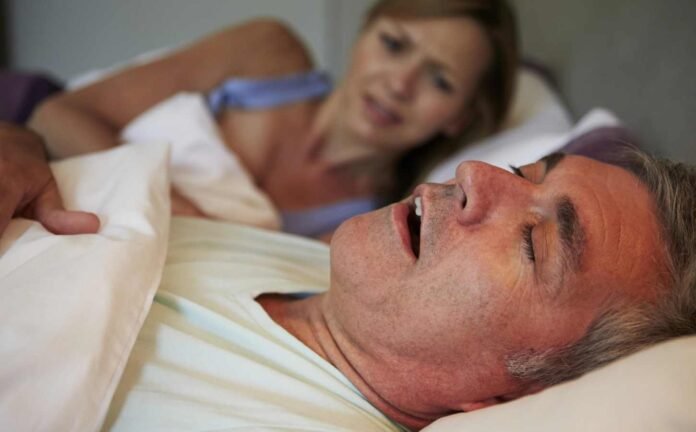 A couple in bed. The man is snoring and the female is half sitting up unable to sleep.