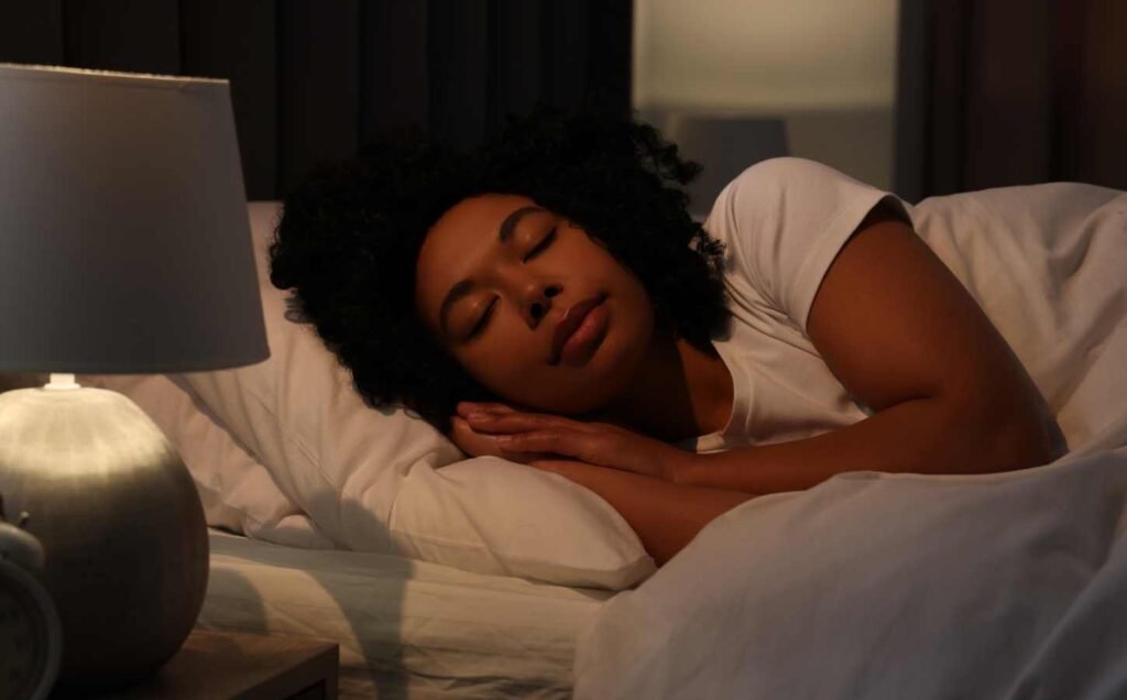 A young female sleeping in a soft bed with a bed lamp on.