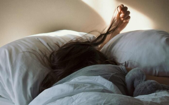 A woman laying face down in bed, awake, playing with her hair because she is probably experiencing sleep disordered breathing.