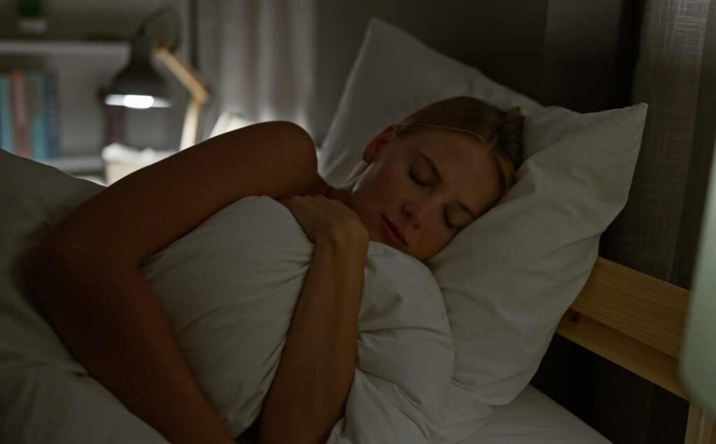 Young blonde woman lying in bed asleep hugging the duvet.