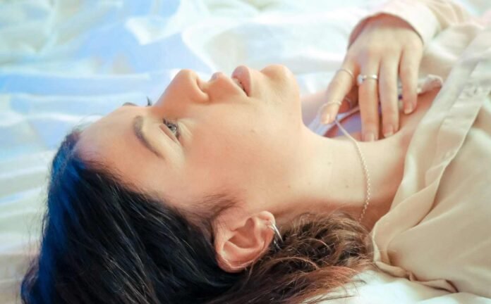 A female with dark hair laying awake on a bed with white sheets, experiencing sleep latency.