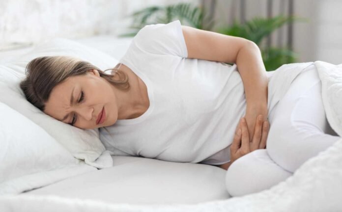 A woman lying on her side in bed suffering from constipation.